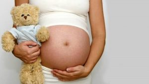 Mulher grávida segurando um urso de pelúcia.