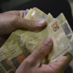 Duas mãos segurando notas de 50 reais