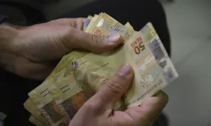 Duas mãos segurando notas de 50 reais